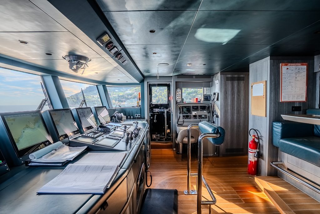 Yacht bridge with navigation screens, control console and helm chair, coastline visible through windows