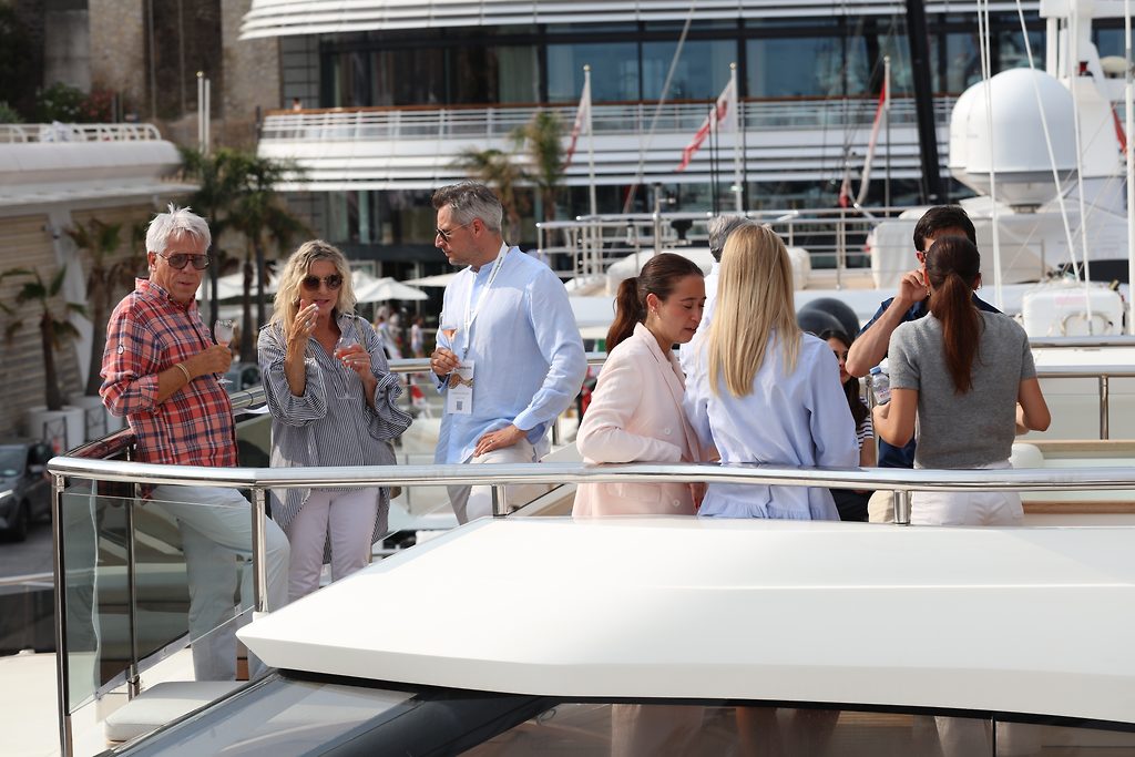 Visitantes reunidos en la cubierta de un yate en un puerto durante un salón náutico