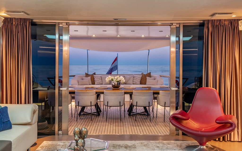 Salón de yate que se abre a una zona de comedor en la cubierta de popa con vista al mar al atardecer