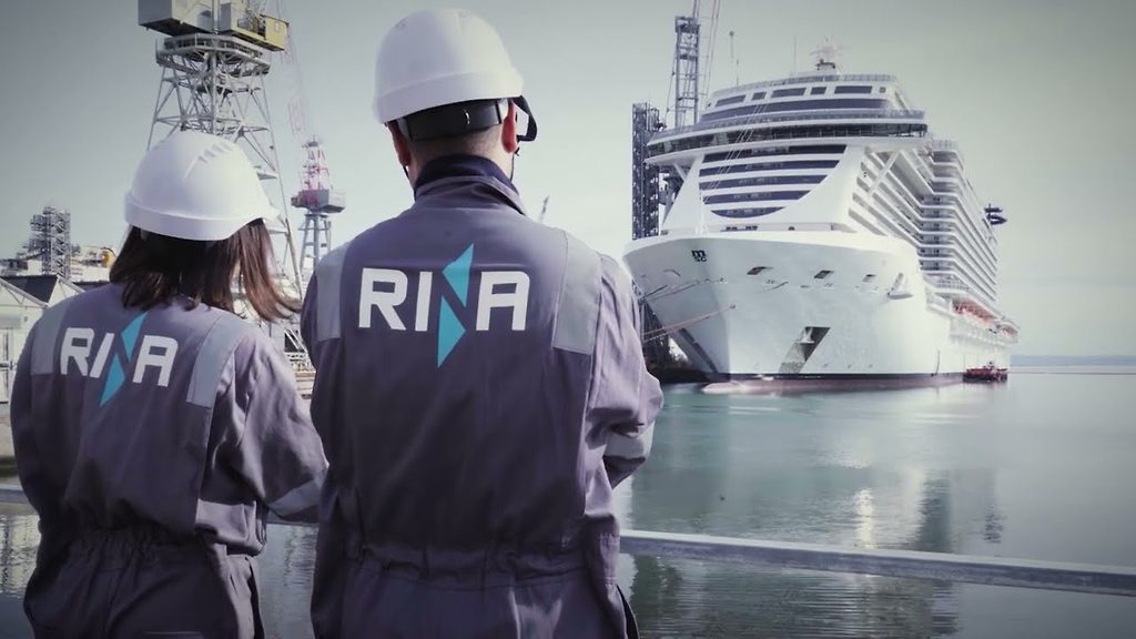 Inspektoren mit Helm und beschrifteter Arbeitskleidung beobachten ein Kreuzfahrtschiff am Werftkai