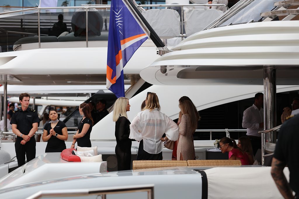 Crew und Besucher stehen im Marina-Hafen zwischen aufliegenden Motoryachten