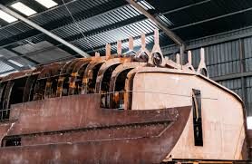 Steel yacht hull under construction with exposed frames, in a boatyard shed