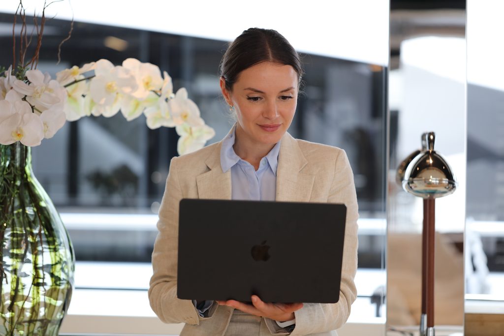 Courtière en yachts travaillant sur un ordinateur portable dans un bureau avec orchidées et lampe chromée