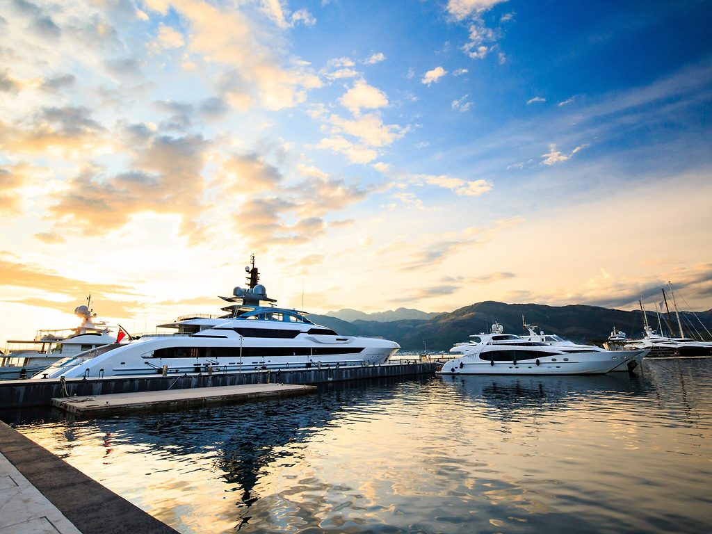 Motor yachts moored in a marina at sunset, mountains in the background