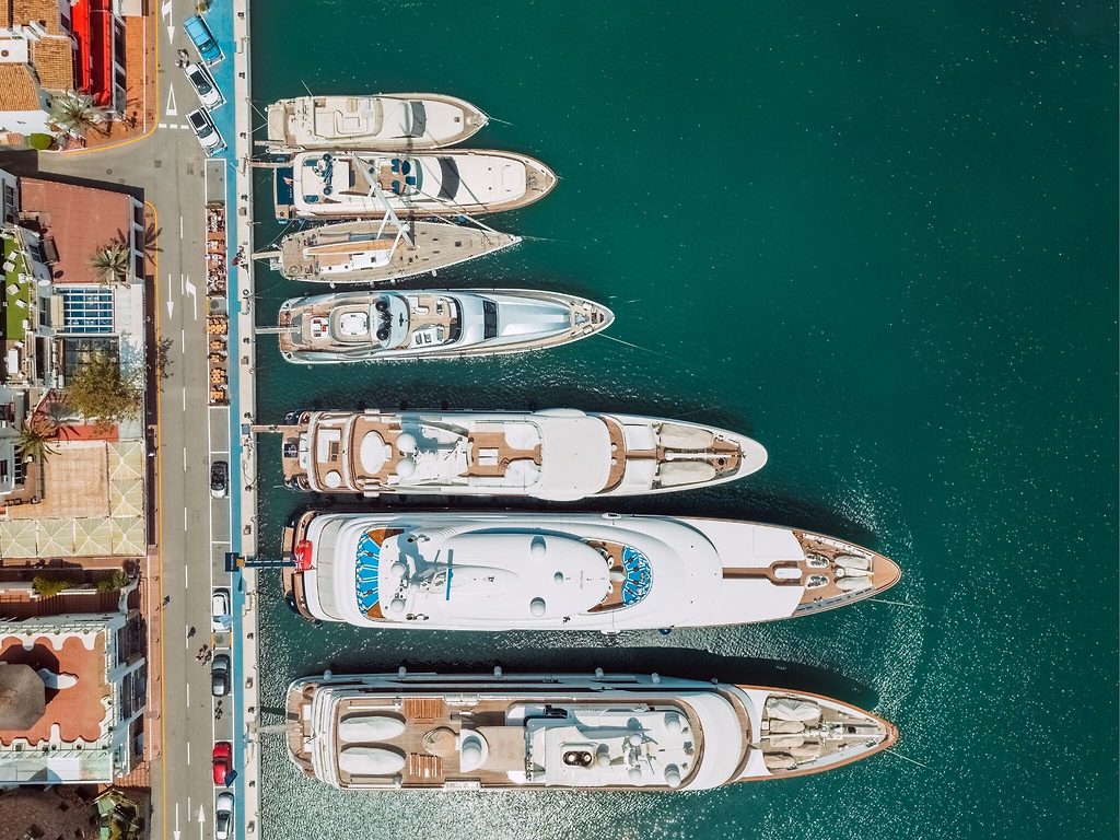 Aerial view of superyachts moored side by side along a marina promenade