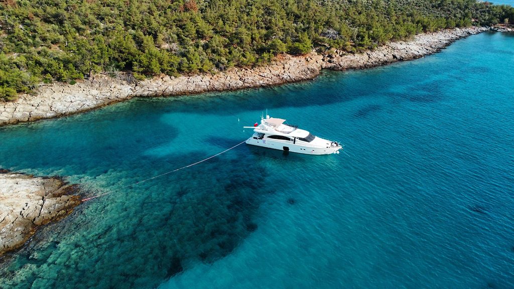 Motoryacht vor Anker nahe einer felsigen, pinienbewachsenen Küste in klarem türkisem Wasser