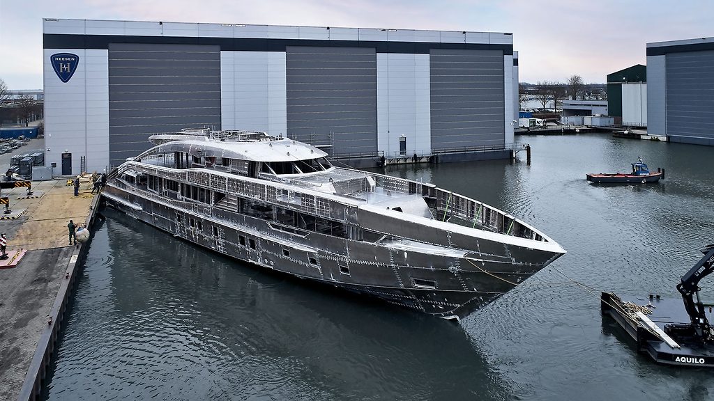 Casco de superyate sin pintar a flote junto a un hangar del astillero, en construcción