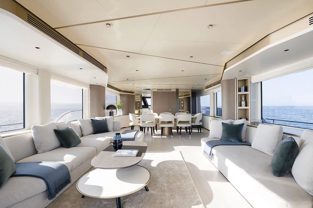 Salon de yacht avec canapés et table à manger, mer visible par les fenêtres des deux côtés