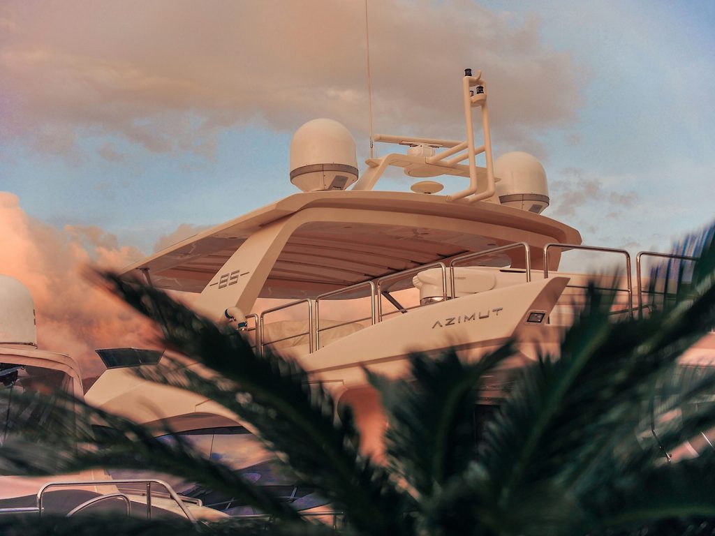 Oberdeck einer Azimut-Motoryacht mit Radar und Antennen, bei Sonnenuntergang vertäut, Palmwedel im Vordergrund