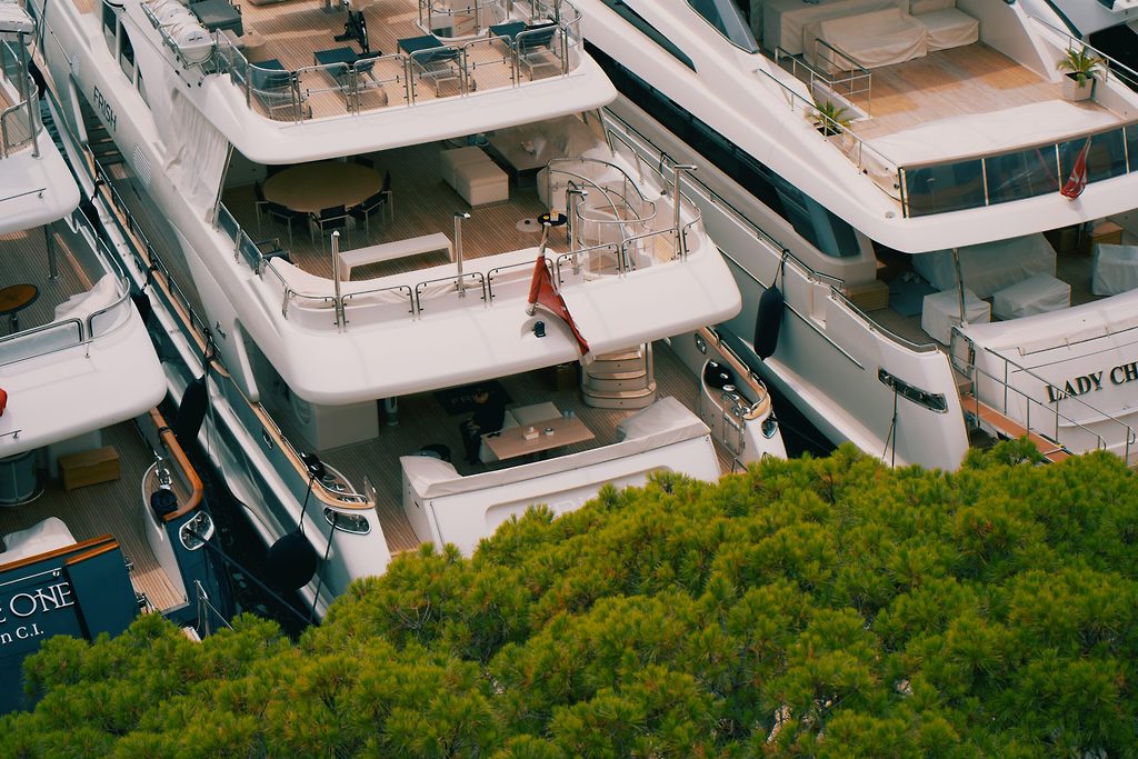 Superyachten heckseitig im Hafen vertäut, von oben durch Baumkronen gesehen