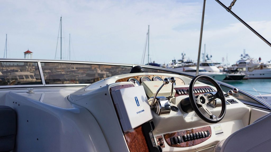 Poste de pilotage et volant d'un yacht à moteur, avec d'autres yachts amarrés dans un port en arrière-plan