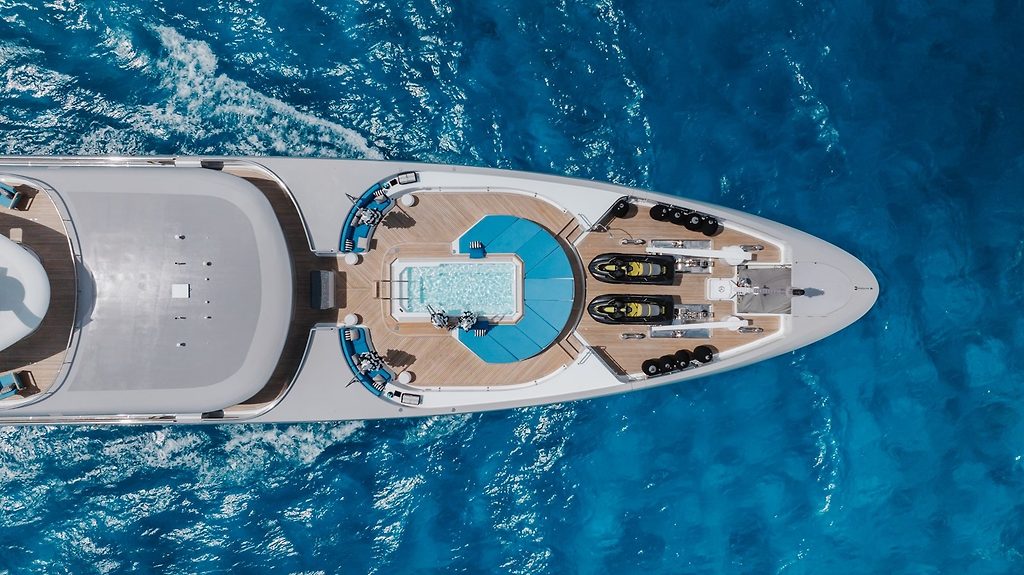 Aerial view of a superyacht's bow deck with pool and jet skis, underway at sea
