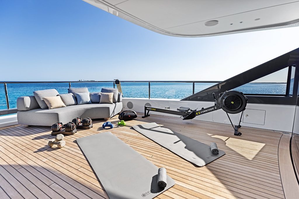 Fitness area with rowing machine and yoga mats on a yacht's deck, sofa lounge and sea view