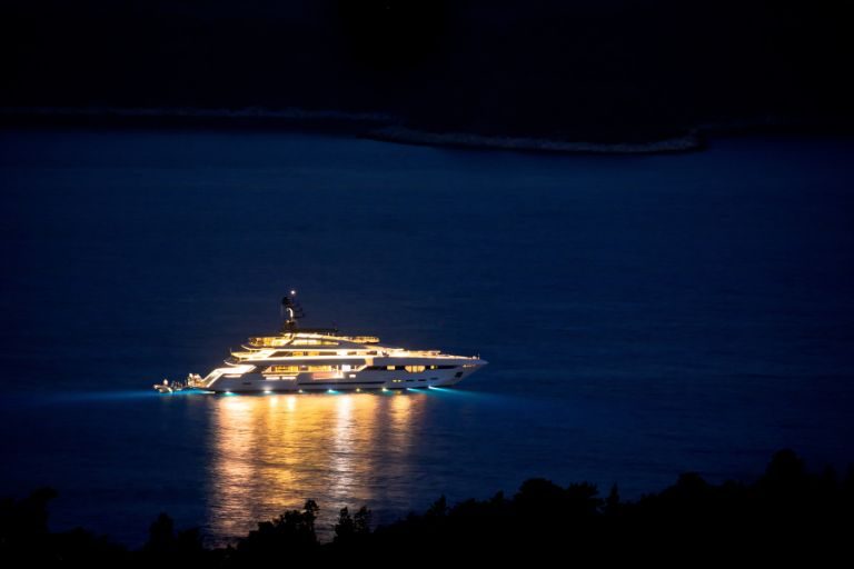 Yate a motor iluminado de noche, anclado en una bahía con reflejos de luz en el agua