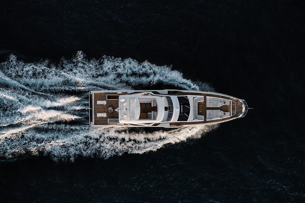 Aerial view of a motor yacht cruising at speed, leaving a wide wake on dark water