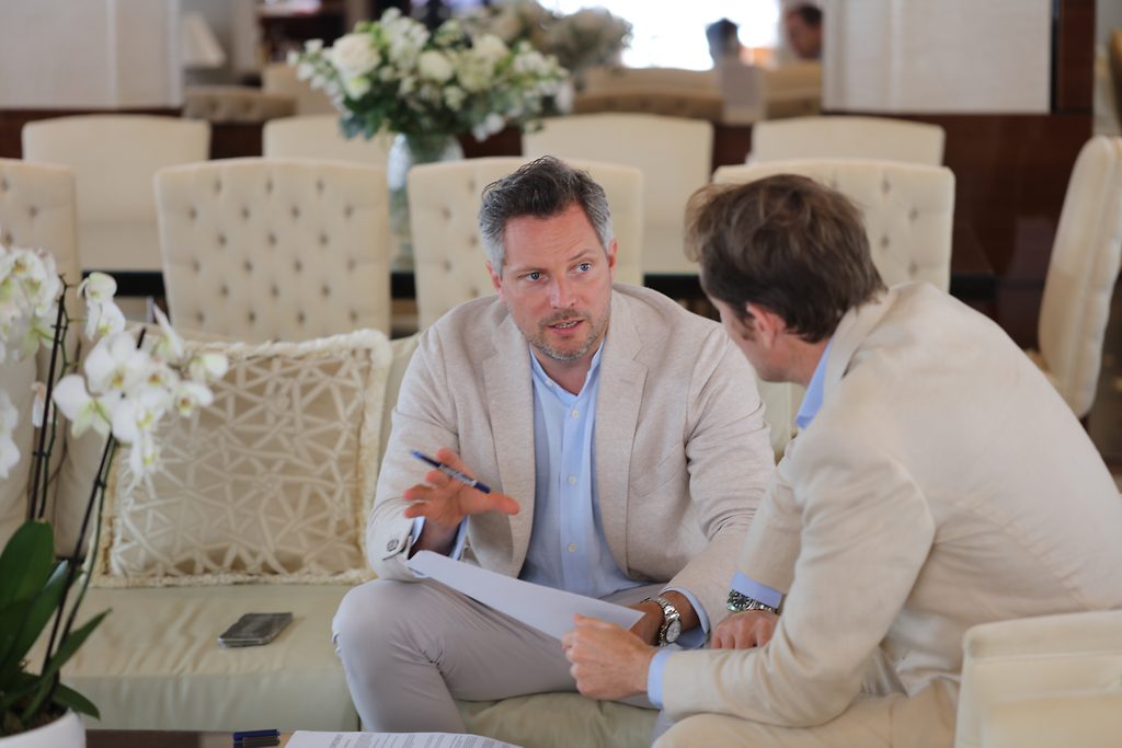 Due uomini seduti su un divano mentre esaminano documenti relativi a un contratto d'acquisto di yacht