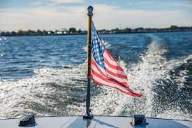 Amerikanische Flagge am Heckmast einer Yacht, mit Kielwasser und Küste im Hintergrund