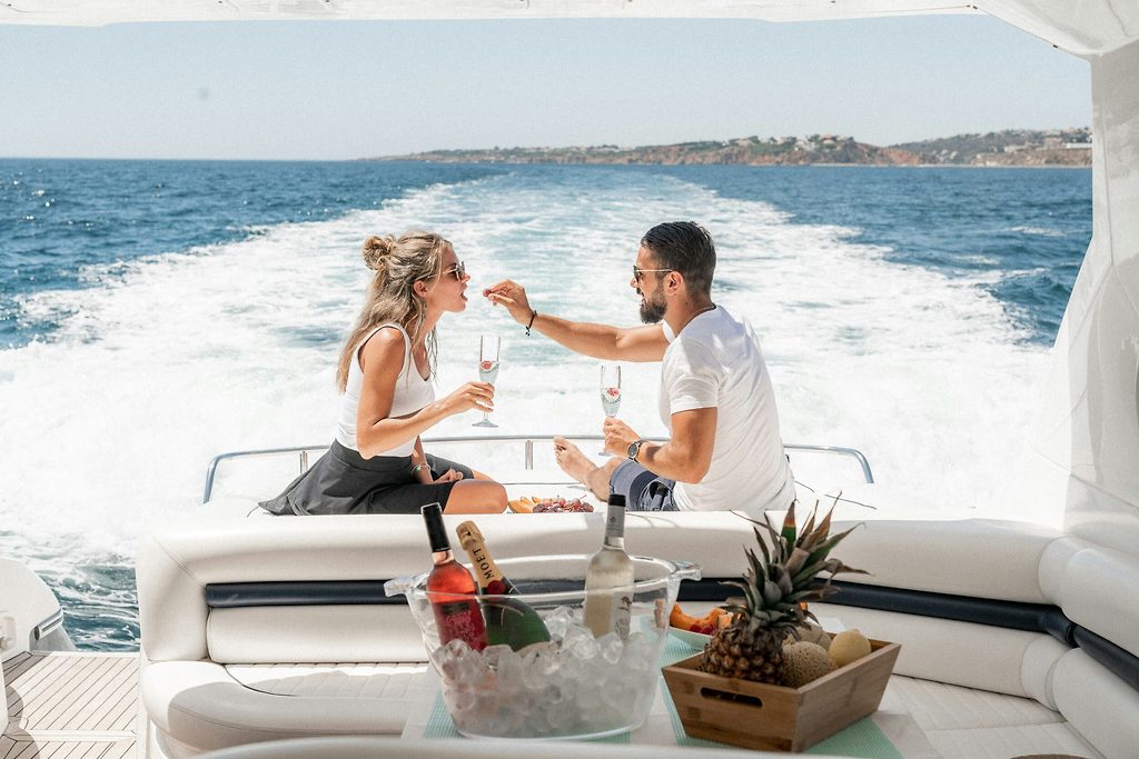 Pareja con champán y fruta en la cubierta de popa de un yate a motor navegando