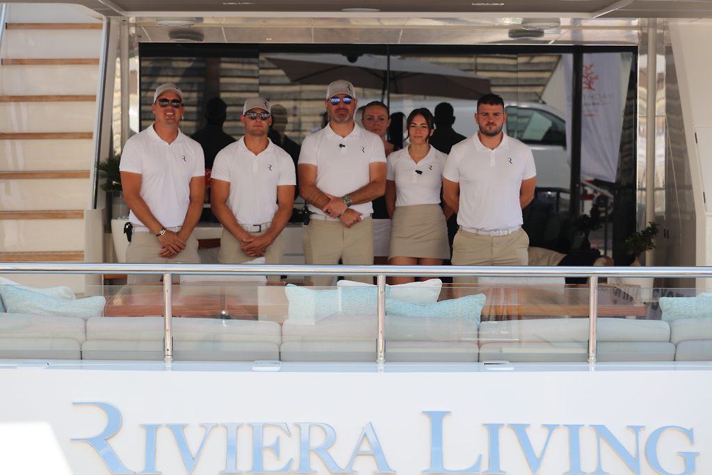 Yacht crew standing in matching uniforms on the aft deck of a motor yacht named Riviera Living