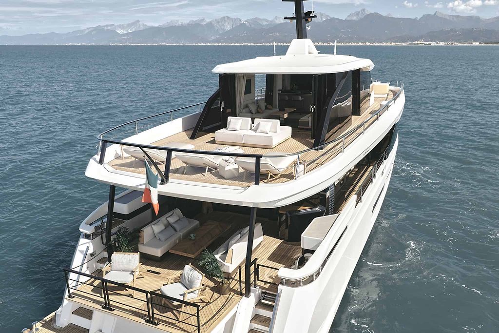 Motor yacht with multiple deck lounges, anchored near a coastline with mountains