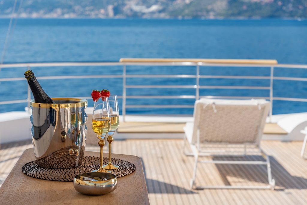Champagne bucket and glasses with strawberries on a yacht's deck table, sea in the background