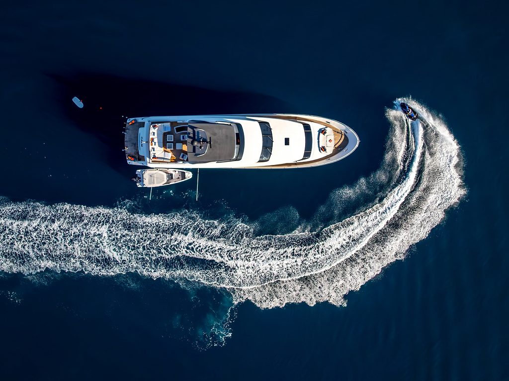 Aerial view of a motor yacht at anchor with a jet ski circling and carving wake patterns