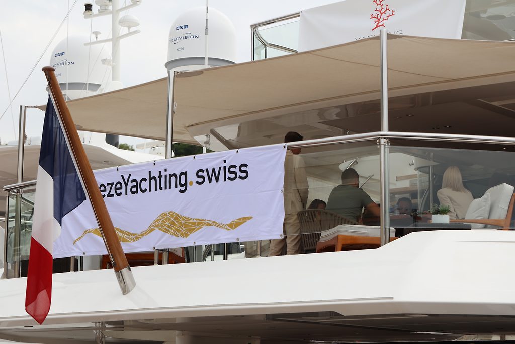 Французский флаг и баннер breezeYachting.swiss на верхней палубе яхты с людьми, сидящими под тентом