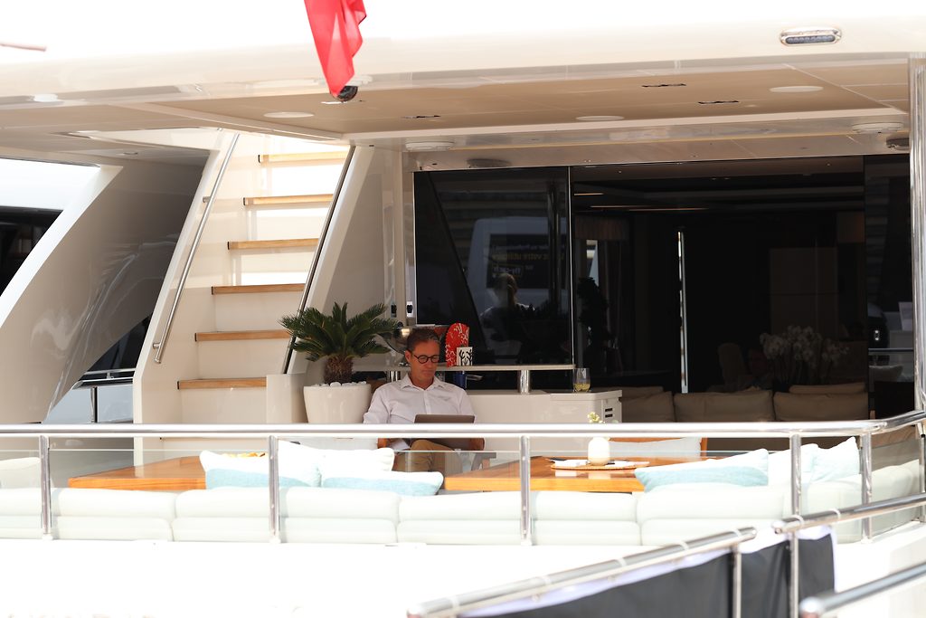 Mann arbeitet am Laptop auf dem Achterdeck einer Motoryacht