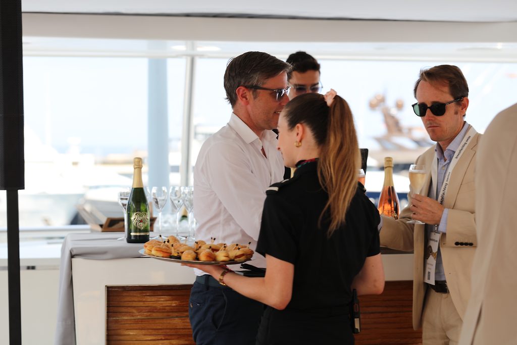 Miembro de la tripulación sirviendo canapés a invitados en la cubierta de popa de un yate durante un evento en el puerto