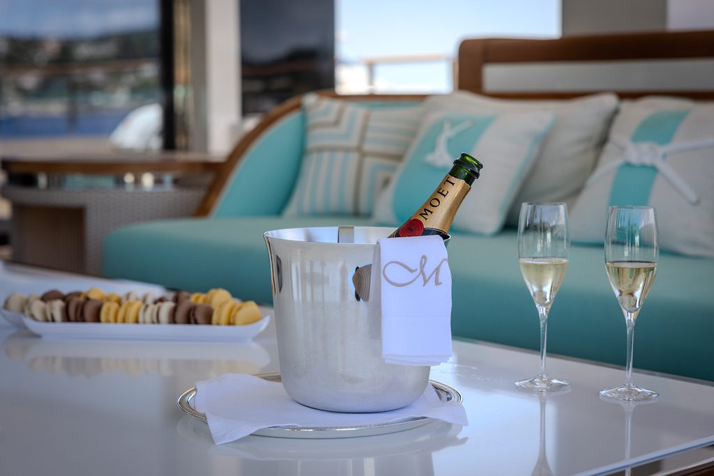 Botella de champán enfriándose en una cubitera con dos copas y macarons sobre la mesa de la cubierta de popa de un yate