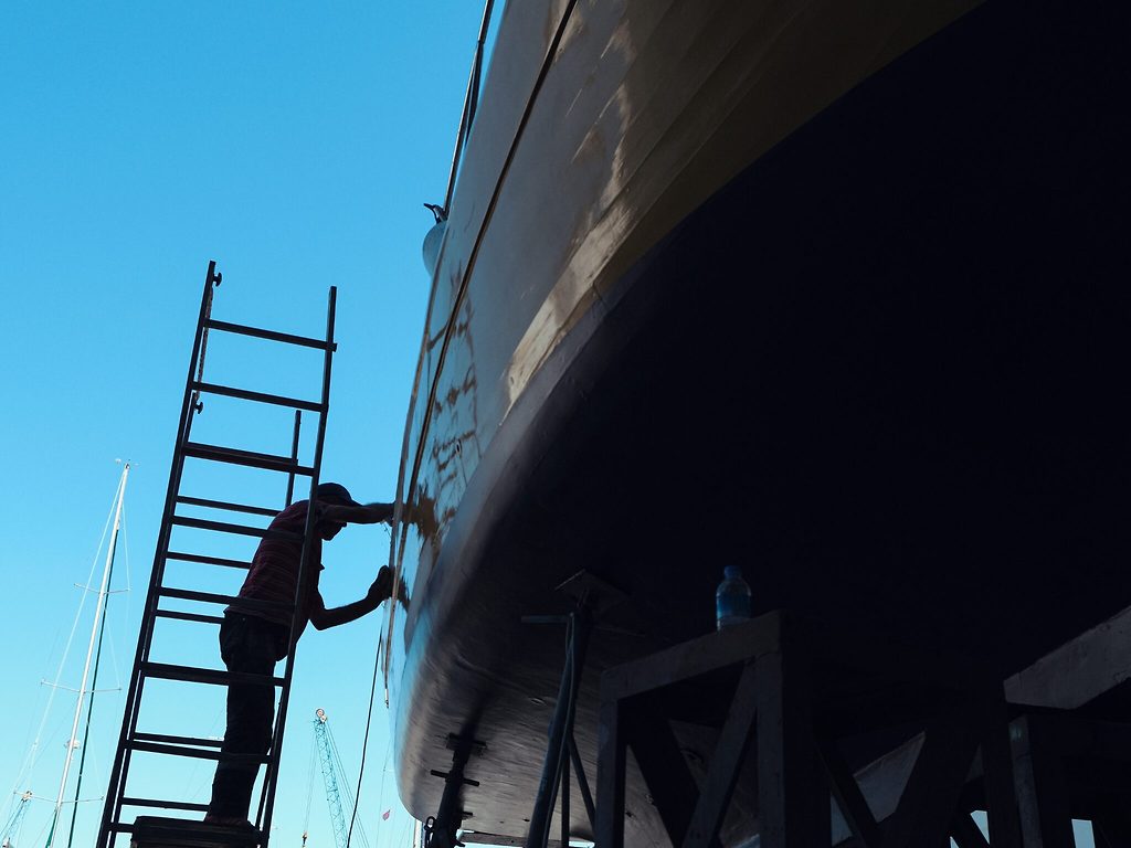 Trabajador en una escalera lijando el casco de un yate en dique seco