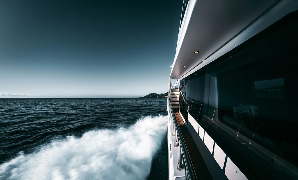 Ponte laterale e scia di uno yacht a motore, in navigazione lungo una costa