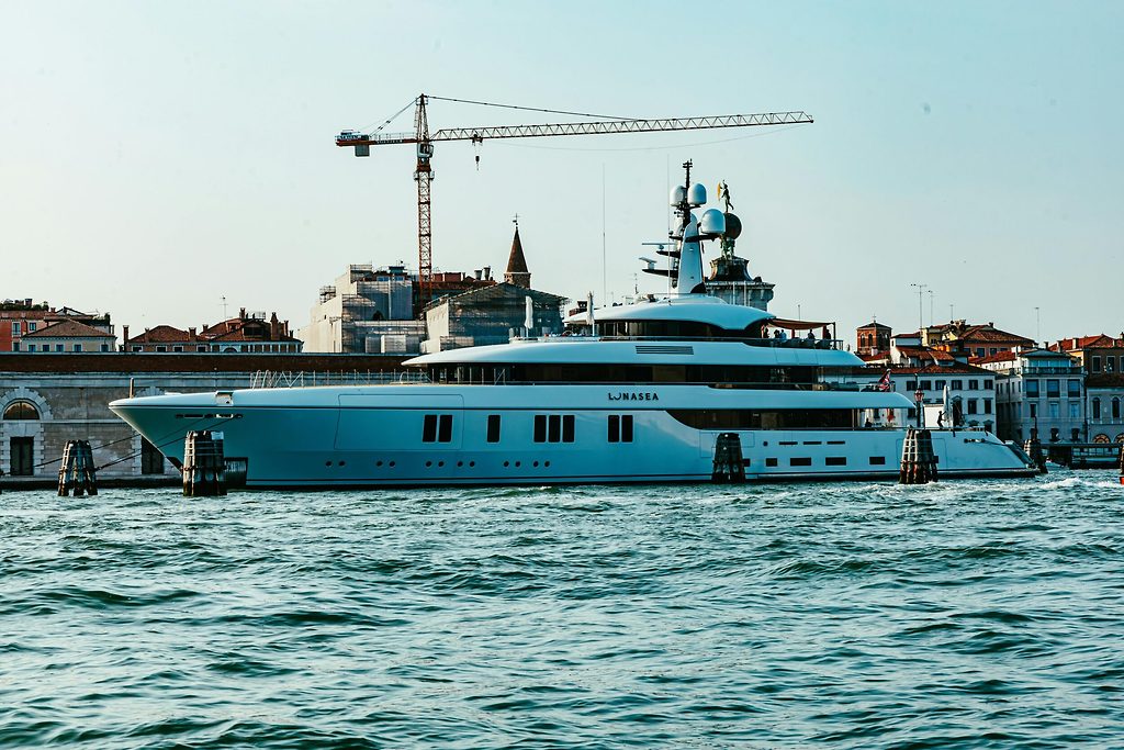 Superyacht moored near a historic city waterfront with a crane in the background