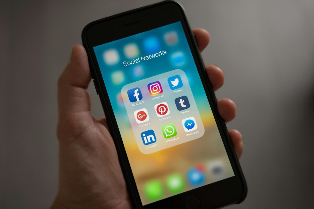 Mano sosteniendo un smartphone que muestra una carpeta de iconos de aplicaciones de redes sociales