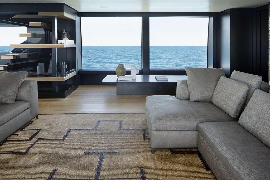 yacht saloon with grey sofas and shelving unit, large windows overlooking the sea