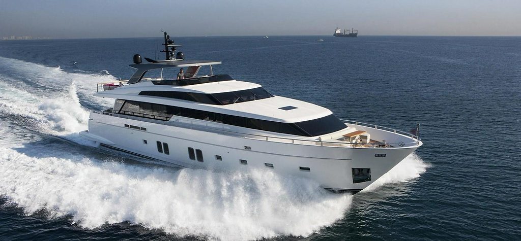Sanlorenzo SL106 motor yacht cruising at speed on open sea, cargo ship in background