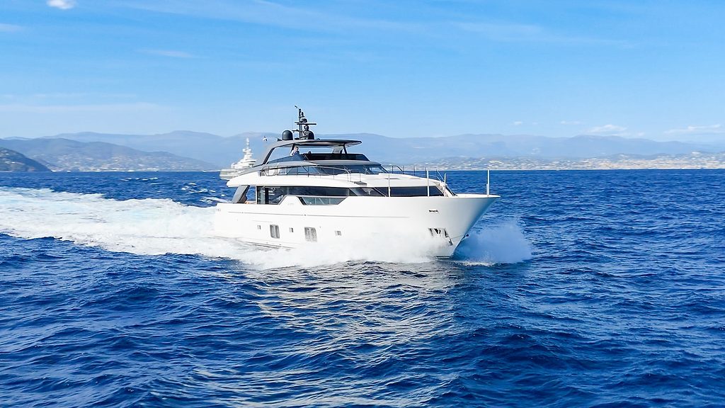 Yate a motor navegando a velocidad en mar abierto, montañas en el horizonte