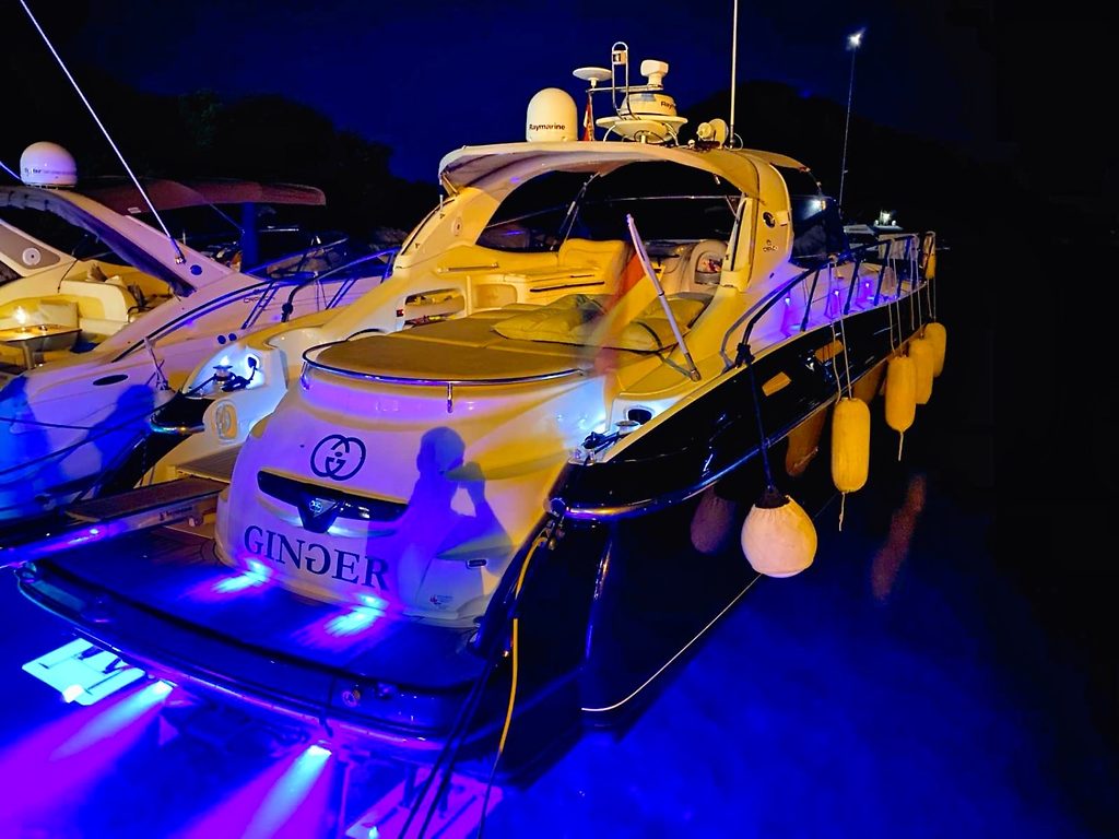 Motor yacht named Ginger moored at a marina berth at night, lit by blue underwater lights