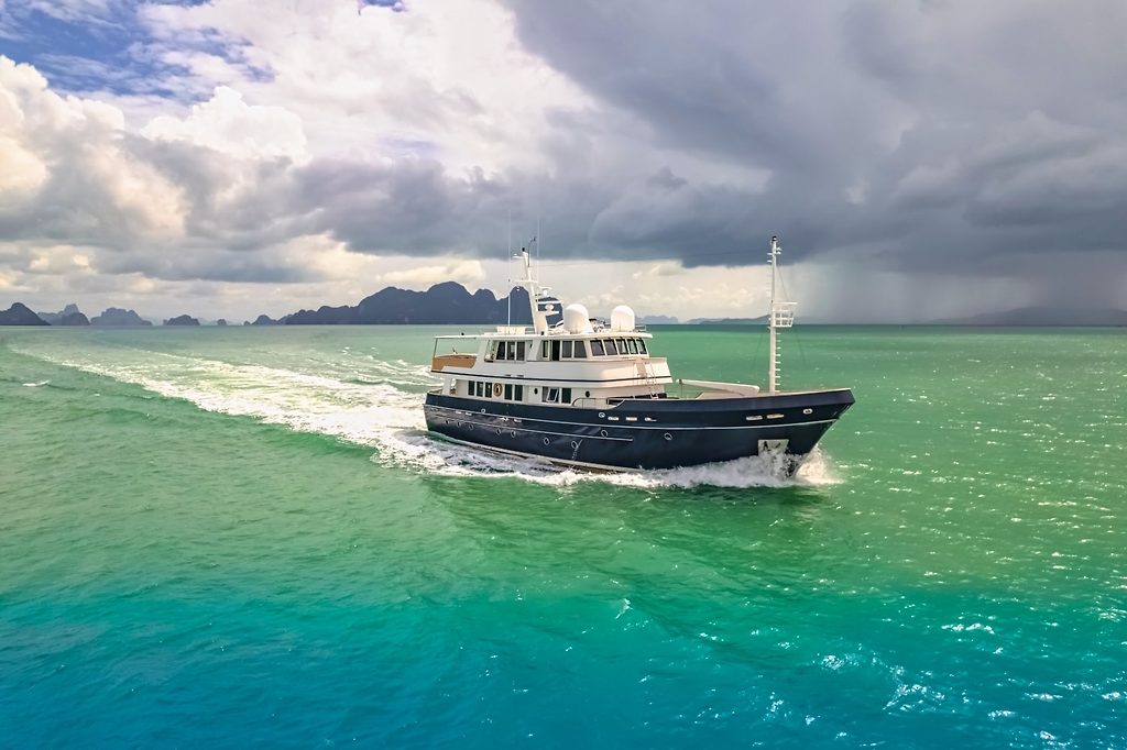 Expeditionsyacht auf türkisfarbenem Wasser nahe tropischen Inseln unter stürmischem Himmel