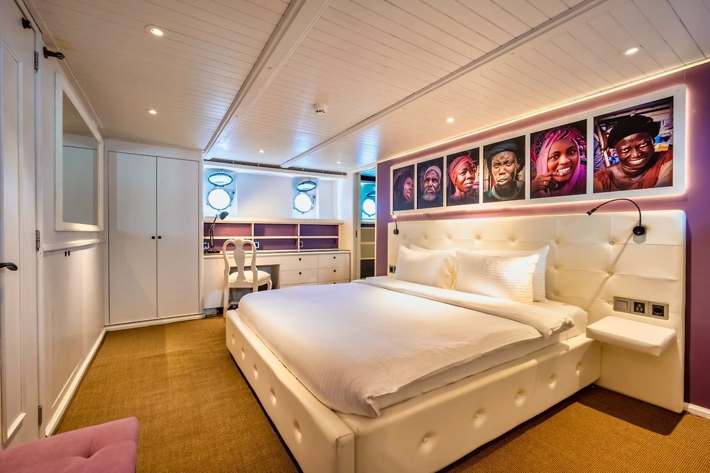 Gästekabine mit weiss gepolstertem Bett und Porträtfotos über dem Kopfteil, auf einer Yacht