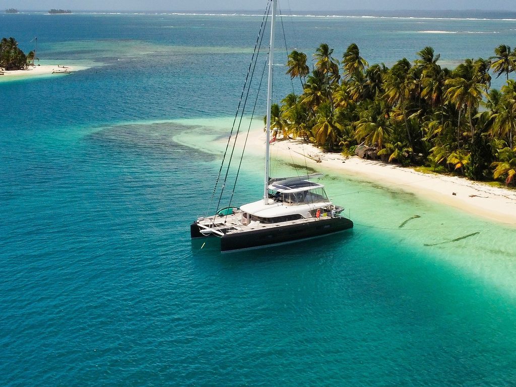 Catamarano a vela ancorato vicino a un'isola tropicale bordata di palme