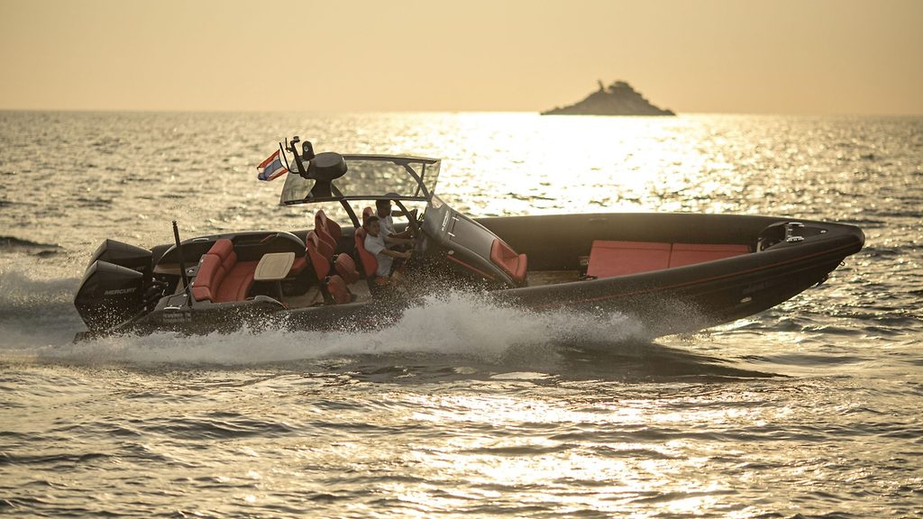 Schnelles Schlauchboot fährt bei Sonnenuntergang an einer felsigen Insel vorbei