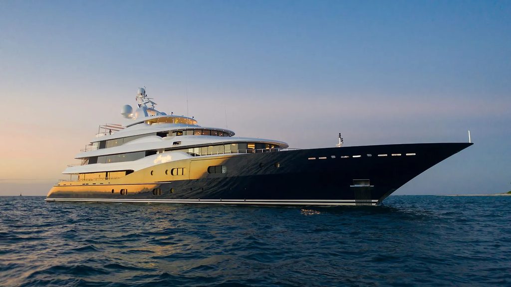 Superyacht à coque noire et dorée à l'ancre en mer au coucher du soleil