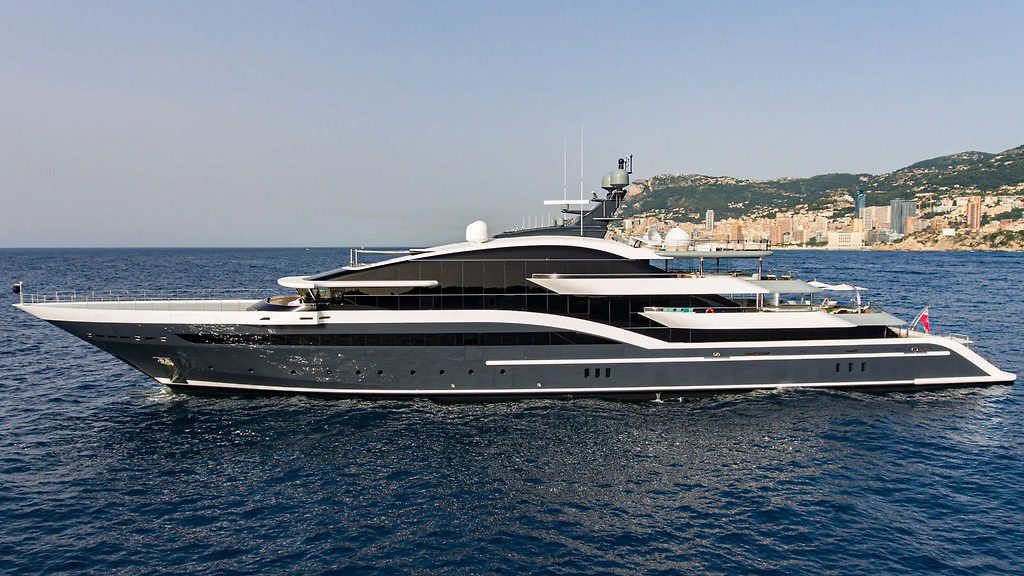 Superyacht naviguant près de la côte, avec une ville en coteau en arrière-plan