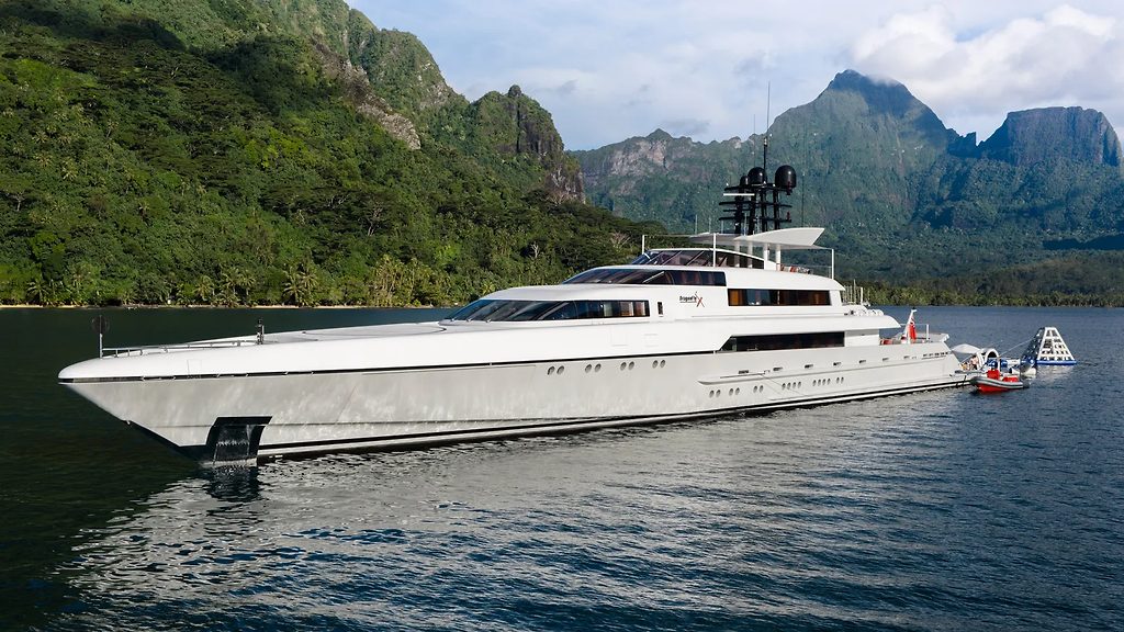 Yacht à moteur ancré près d'une annexe, avec des montagnes verdoyantes en arrière-plan