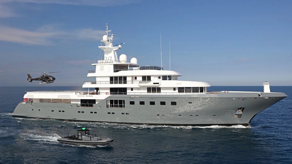 Yacht explorateur naviguant en mer, escorté d'un hélicoptère et d'une annexe