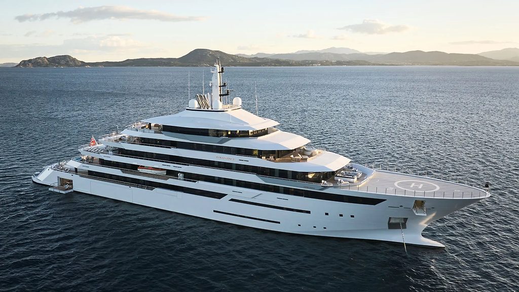Grand yacht à moteur avec héliport ancré près d'une côte au crépuscule