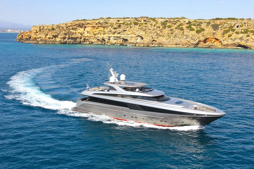 Yacht à moteur naviguant à vive allure le long d'une côte rocheuse, laissant un sillage courbe