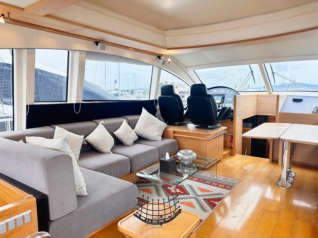 Salón de yate con asientos grises, mesa de cristal y sillas de timón, amarrado en un puerto deportivo