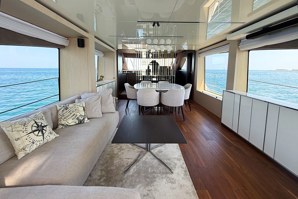 Saloon with lounge seating and dining table on a motor yacht, sea visible through windows
